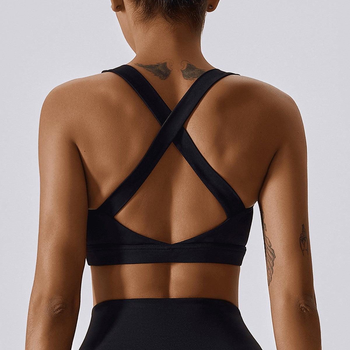 Back view of a woman wearing a black Urban Fashion & Streetwear | Craftklart compression sports bra with cross straps.