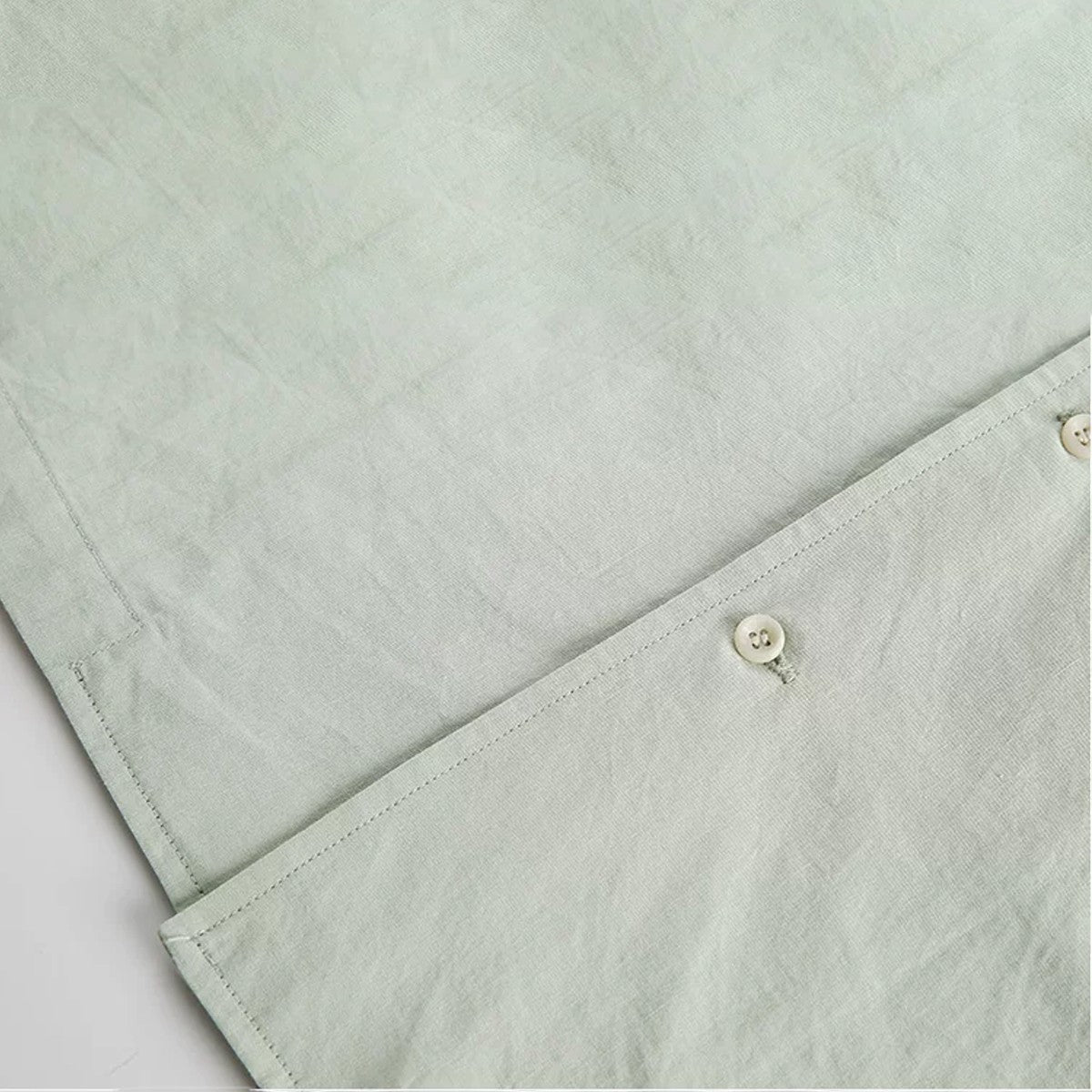 Close-up of light green cotton fabric with clean stitching and a button from an Urban Fashion & Streetwear | Craftklart shirt